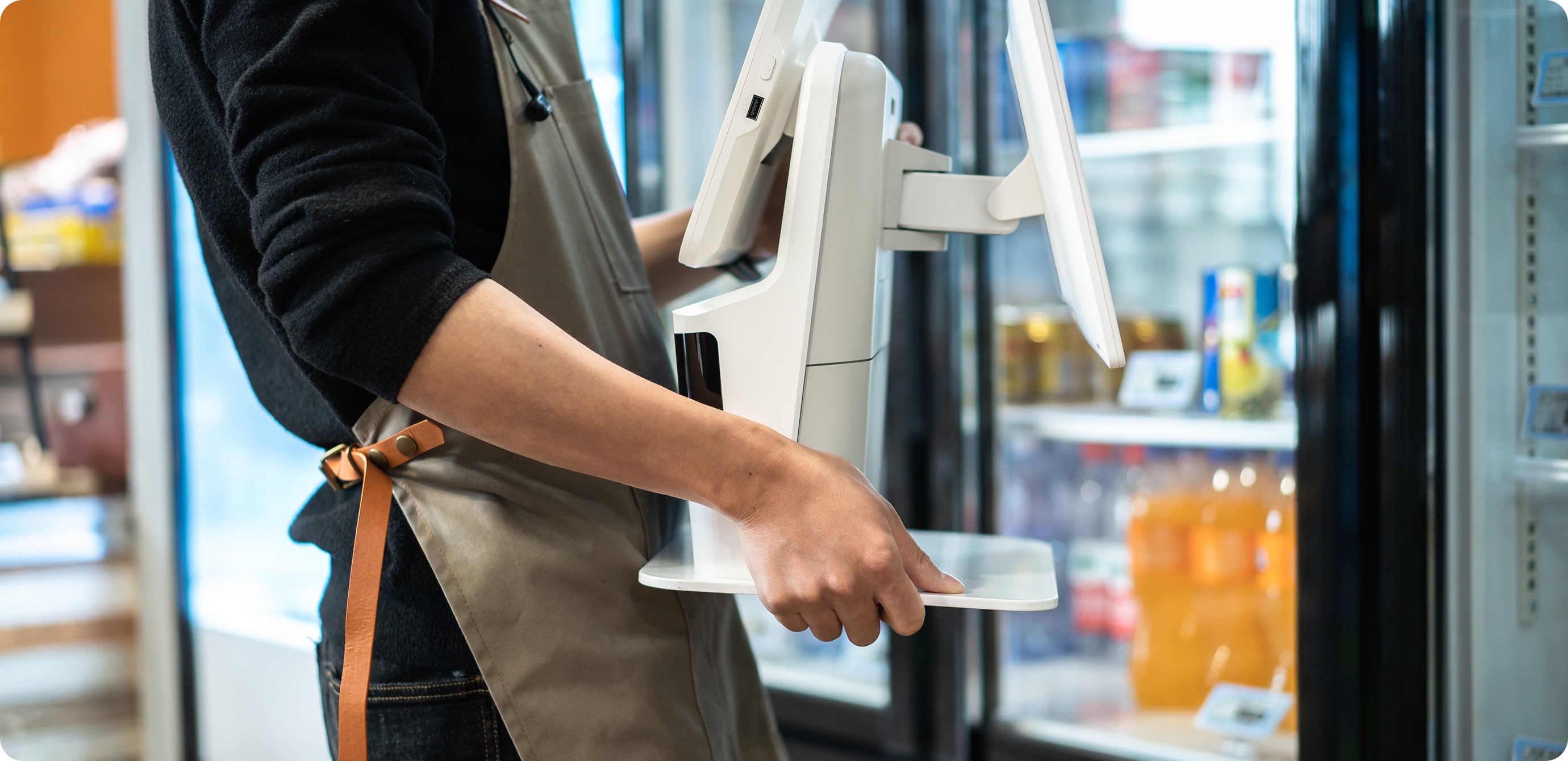 Store staff member carrying the compact, all-in-one Sunmi K2 Mini kiosk by hand inside a convenience store