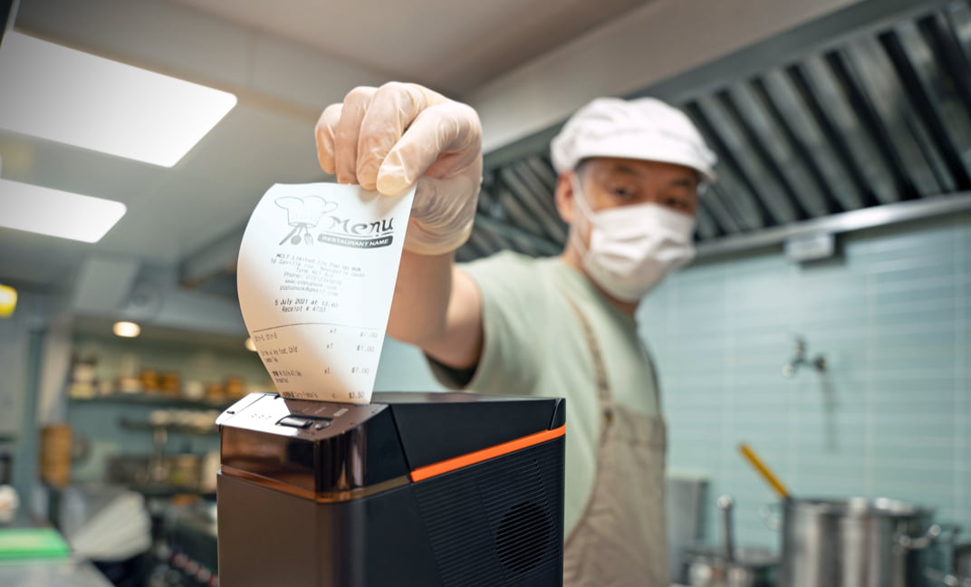Kitchen staff pulling a freshly printed receipt from the Sunmi printer