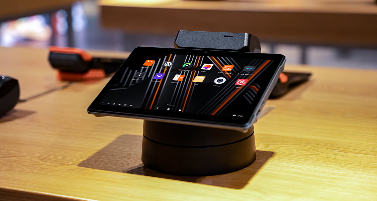 Sunmi V3 MIX docked on a rotating base showing the home screen at a counter